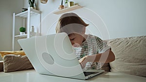 Child learning to typing and using laptop, sitting on sofa at home