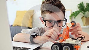 Child learns coding and programming on a laptop. Boy looks with concentration at the robot car and fixes the control