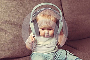 The child learns the world. A little happy child is sitting on the bed in big headphones and listening to music