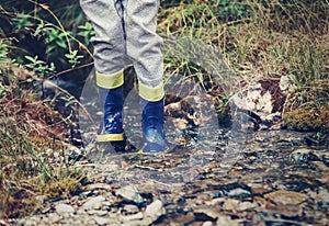 Child legs in gum boots into the forest creek