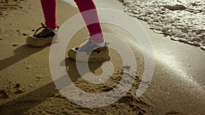 Child legs walking beach water at sea shore. Little girl dance at crashing waves