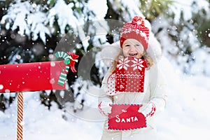 Child with letter to Santa at Christmas mail box in snow
