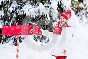 Child with letter to Santa at Christmas mail box in snow