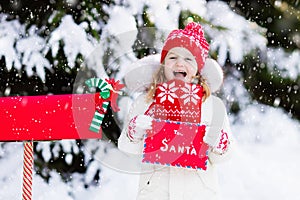 Child with letter to Santa at Christmas mail box in snow