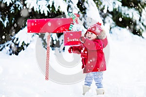 Child with letter to Santa at Christmas mail box in snow