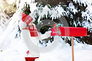 Child with letter to Santa at Christmas mail box in snow