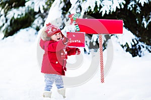 Child with letter to Santa at Christmas mail box in snow