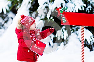 Child with letter to Santa at Christmas mail box in snow