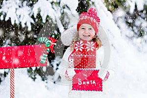 Child with letter to Santa at Christmas mail box in snow