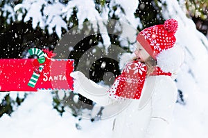 Child with letter to Santa at Christmas mail box in snow