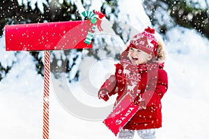 Child with letter to Santa at Christmas mail box in snow