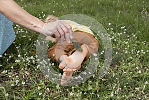 child lies on the grass, mother gently tickles his bare feet