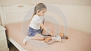 The child listens to the doll with a stethoscope, sits on the bed.