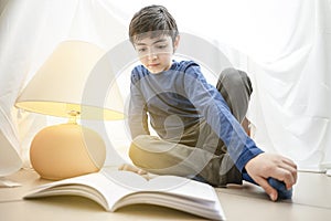 Child little boy reading a magic book in a tent at home