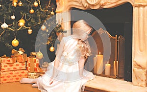 Child little girl with gifts boxes near christmas tree and fireplace home