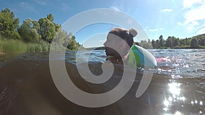 A child, a little girl, learns to swim in the river and swims through the water in inflatable armbands on a sunny summer