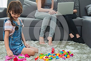 child a little girl is playing blocks at home. Mother with friend working on laptop or shopping online