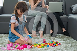 child a little girl is playing blocks at home. Mother with friend working on laptop or shopping online