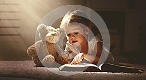Child little girl reading a magic book in dark home