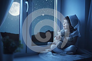 Child little girl at window dreaming and admiring the starry sky