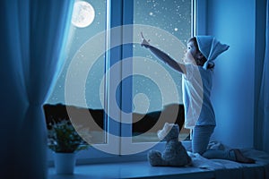 Child little girl at window dreaming and admiring starry sky at