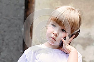Child, little kid speaking on mobile phone alone. Young girl holding a smartphone next to her ear talking, closeup