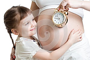 Child looking at alarm clock and pregnant woman belly