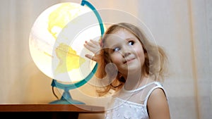 Child looking on the globe and world. Baby girl looks at the map and showing the place of the future journey