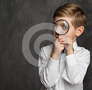 Child looking through Magnifying Glass over Dark Background. Intelligent School Boy with Magnifier Lens. Kid Eye Care and Eyesight