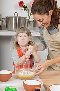 Child looking and whipping to make a cake with mother