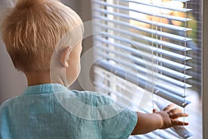 Child looking at window through the blinds. Self-isolation, quarantine in outdoors