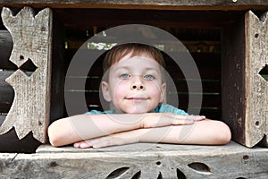 Child looking through window opening of wooden house