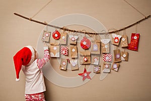 Child looks at the advent calendar. Baby girl in a Christmas hat and pajamas shows on first gift