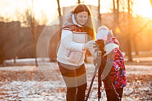 Child looks at the camera, takes pictures with tripod together with his mother at sunset