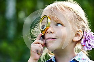 The child looks through a magnifier. Beautiful little girl looking through a magnifying glass