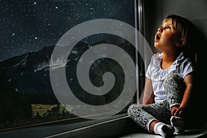 child looks out the window into the night sky