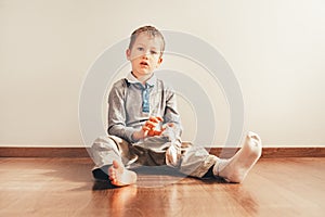 Child with lots of independence sitting on the floor putting on his socks with an expression of effort