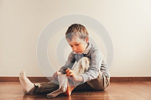 Child with lots of independence sitting on the floor putting on his socks with an expression of effort