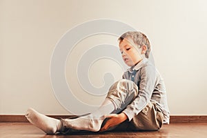 Child with lots of independence sitting on the floor putting on his socks with an expression of effort