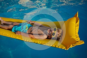 Child lounges on a yellow inflatable raft in swimming pool