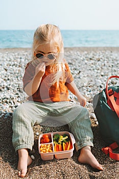 Child with lunch box outdoor eating vegan food on beach healthy lifestyle summer vacations kid girl with lunchbox container