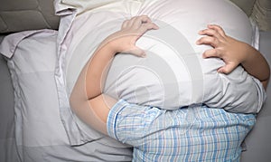 Child lying in bed covering head with pillow