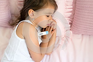 Child is lying in bed with an thermometer with a high temperature