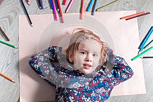 Child lying on the floor paper near crayons. Little girl painting, drawing. Top view. Creativity concept.