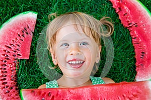 Child lying on the grass with big slice watermelon in summer time. Smiling. Top view.