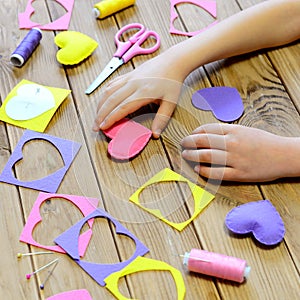 Child made hearts out of felt. Children`s hands on the table. Handmade Valentines day heart gifts, crafts materials and tools