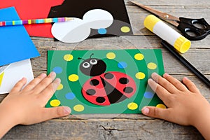 Child made a ladybird from colored paper. Summer card with paper ladybug, stationery on a wooden table. Simple paper circle crafts