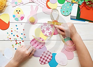 The child makes crafts with his own hands for the Easter. Colorful handmade from multi-colored paper. Scissors, cardboard, eggs,