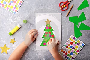 The child makes a greeting card Christmas paper collage. Children`s art project craft for kids