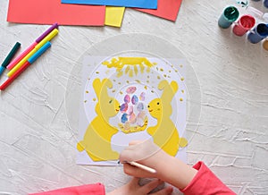 Child making card with Easter bunnies  from colorful paper. Applique. Handmade. Project of children`s creativity, handicrafts,